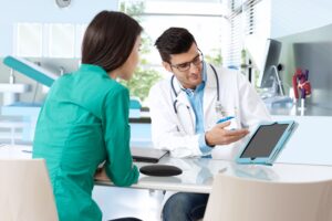 Doctor consulting with female patient, presenting results on tablet computer, sitting at desk.